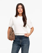 Estelle White short sleeve crewneck sweater styled with dark jeans and a brown suede bag held at the side.