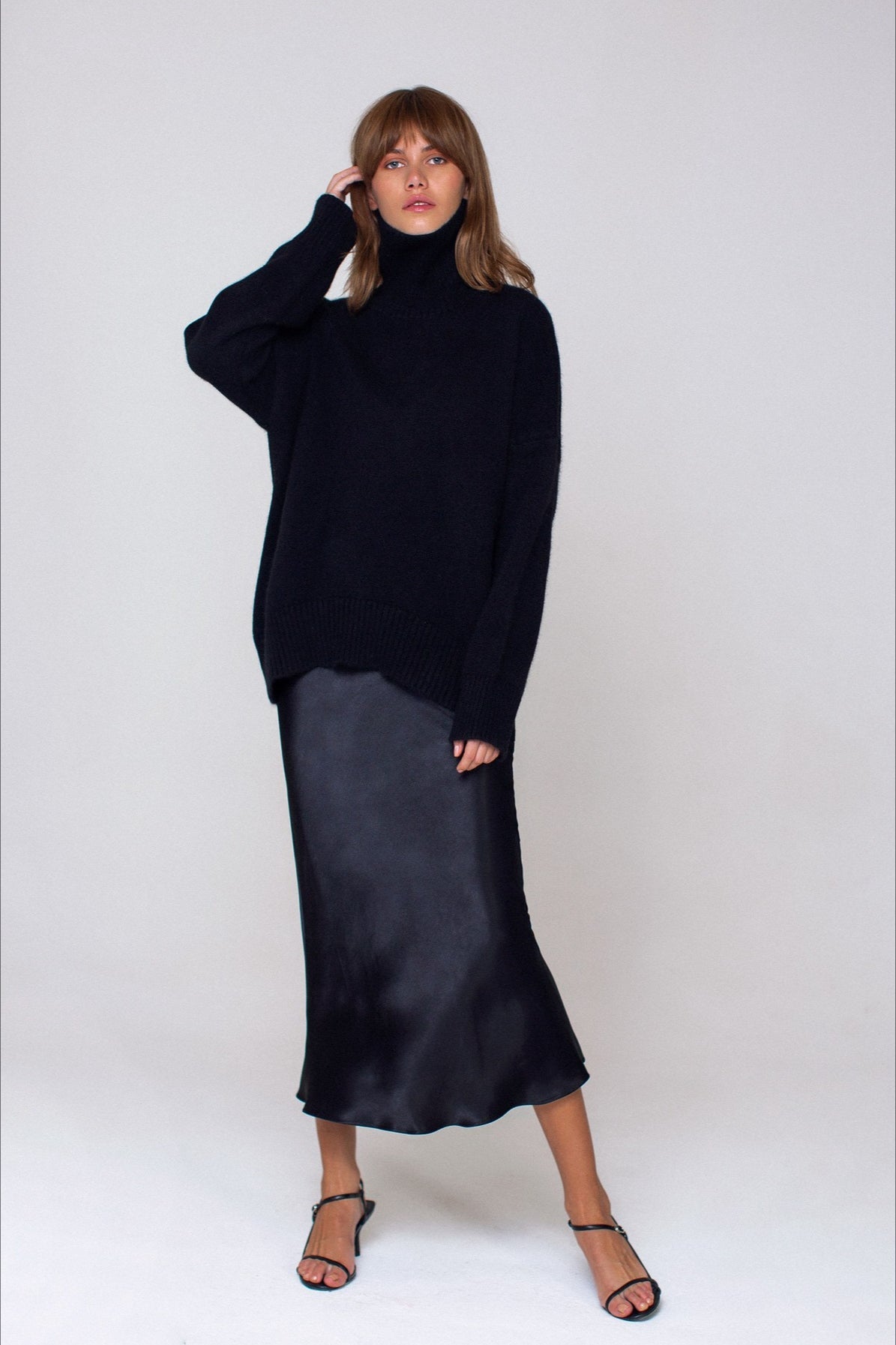 Evelyn Black turtleneck sweater styled with a satin midi skirt and strappy sandals in a full-length view.
