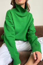 Evelyn Dark Green turtleneck sweater close-up of the ribbed collar and cuffs, styled with white jeans.