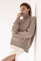 Evelyn Khaki turtleneck sweater shown leaning against a wall, highlighting the ribbed collar, cuffs, and hem.
