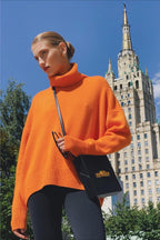 Evelyn Orange turtleneck sweater worn outdoors with black leggings and a black crossbody bag.