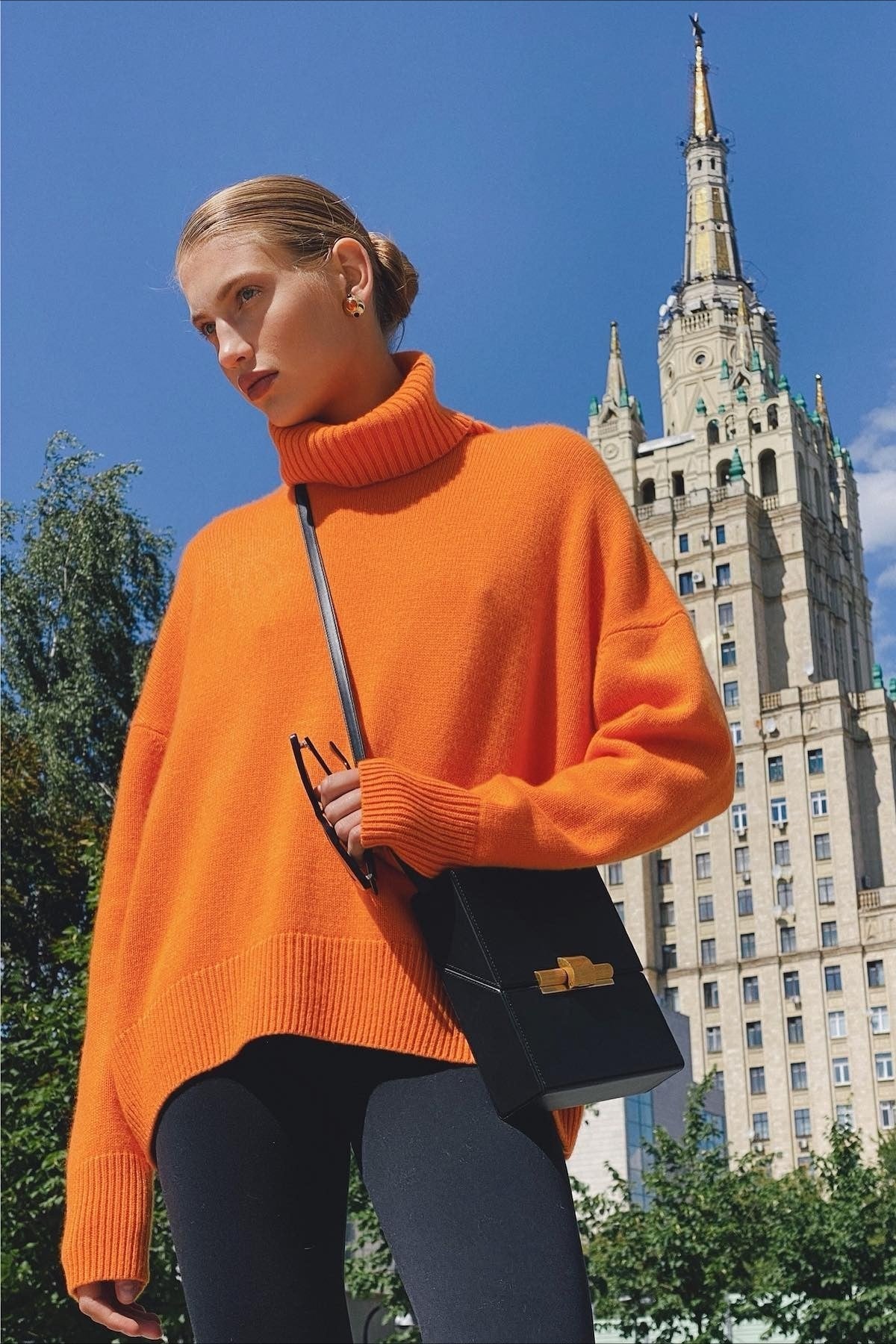 Evelyn Orange turtleneck sweater worn outdoors with black leggings and a black crossbody bag.