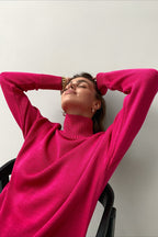 Evelyn Pink turtleneck sweater with arms raised, showing the ribbed turtleneck and ribbed cuffs.