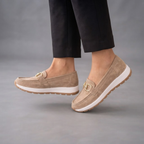 Farrah Sneaker Loafers in Beige Suede with Gold Buckle shown in side view, featuring a soft suede upper, polished gold-buckle detail, slip-on loafer design, lightweight sneaker-inspired sole, cushioned footbed, and versatile everyday silhouette, designed by Bella Hudson.