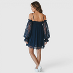 Back view of the Fenella Mini Dress Off-Shoulder Lace Puff-Sleeve Boho in navy blue, highlighting the off-the-shoulder back, sheer lace puff sleeves, and relaxed babydoll silhouette. Designed by Bella Hudson.