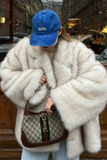 Fiora White faux fur jacket worn open in an oversized fit with wide plush sleeves, styled with a blue cap and light jeans.