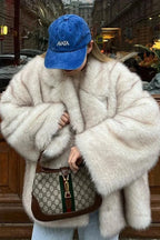 Fiora White faux fur jacket worn open in an oversized fit with wide plush sleeves, styled with a blue cap and light jeans.