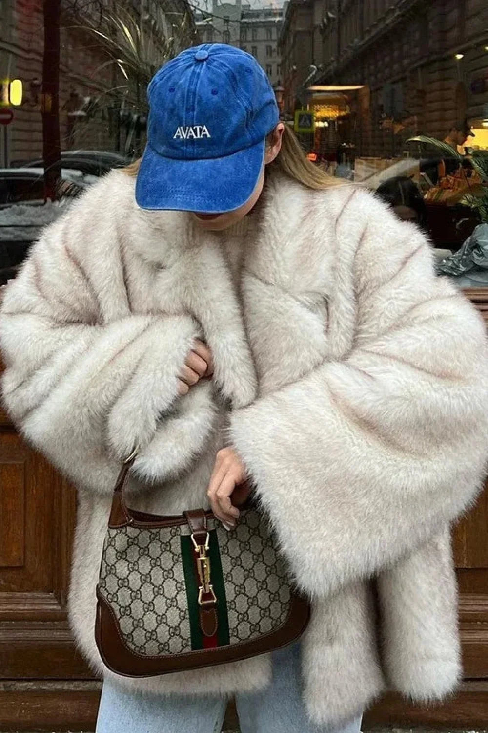 Fiora White faux fur jacket worn open in an oversized fit with wide plush sleeves, styled with a blue cap and light jeans.