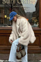 Fiora White faux fur jacket shown from the side with a wide lapel collar and voluminous sleeves, paired with wide-leg light jeans.