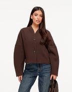 Freya Brown cropped V-neck jacket worn buttoned with two buttons, styled with blue jeans and a brown handbag.