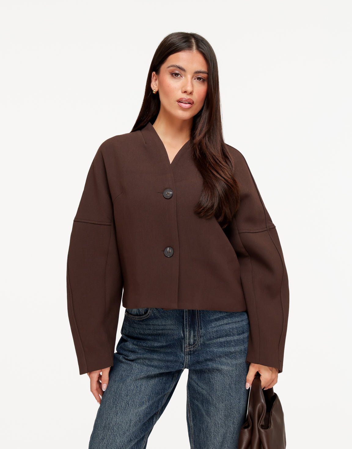 Freya Brown cropped V-neck jacket worn buttoned with two buttons, styled with blue jeans and a brown handbag.