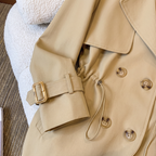Front detail view of the Jennifer Trench Coat Belted Double-Breasted in khaki, highlighting the notched lapels, double-breasted buttons, fitted waist, and structured front construction. Designed by Bella Hudson.