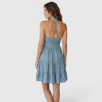 Back view of the Larkin Halter Dress Linen Tiered Bow-Detail in blue, highlighting the halter back, gathered bodice, and softly tiered mini skirt. Designed by Bella Hudson.