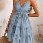 Posing view of the Larkin Halter Dress Linen Tiered Bow-Detail in blue, featuring the halter neckline, bow detail, tiered mini skirt, and lightweight linen construction. Designed by Bella Hudson.