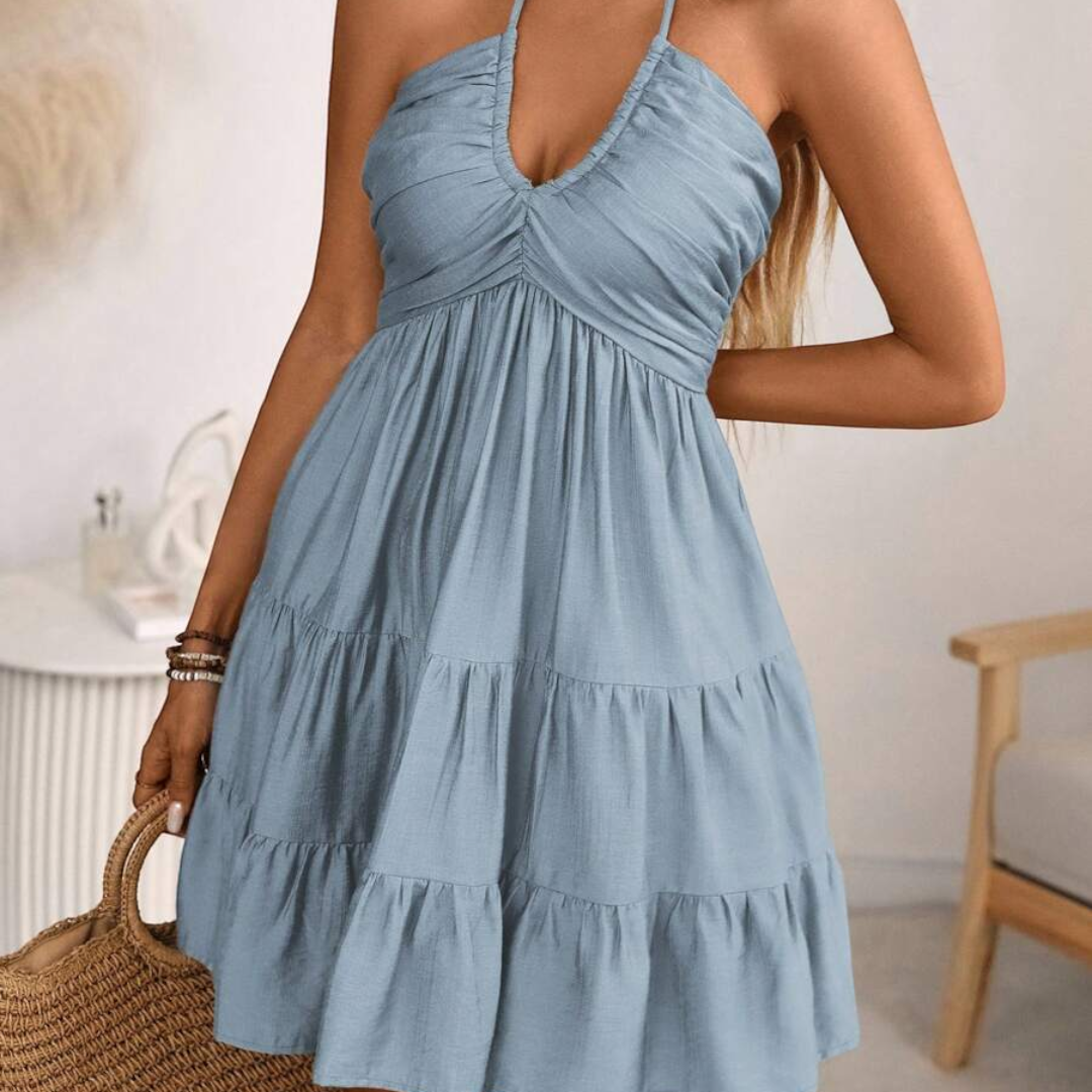 Posing view of the Larkin Halter Dress Linen Tiered Bow-Detail in blue, featuring the halter neckline, bow detail, tiered mini skirt, and lightweight linen construction. Designed by Bella Hudson.