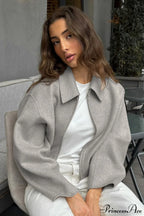 Lena Gray cropped jacket shown seated with a turn-down collar, relaxed silhouette, long sleeves, and zip-front closure
