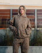 Lena Leopard hoodie set worn by a model standing with hands in the front pocket in front of a wood fence.