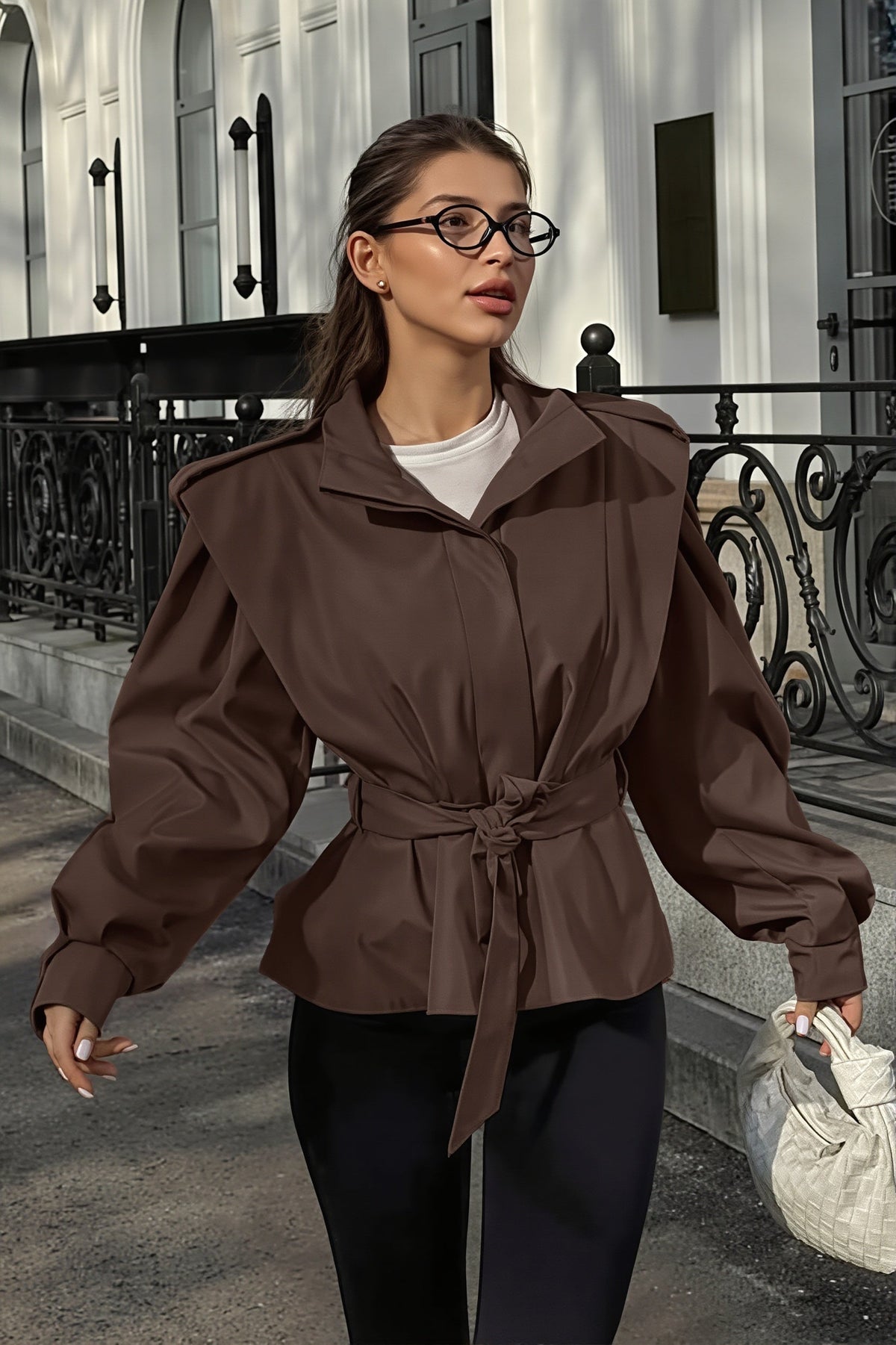 Leona Brown belted peplum jacket worn open at the collar over a white tee with black pants while walking outdoors.