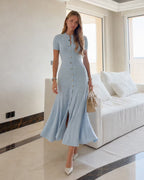 Leonie Blue knit maxi dress showing the flared hem and front slit with a beige handbag.