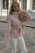 Lila Pink double-breasted short jacket styled with the belt tied at the waist and white trousers on a cobblestone street.
