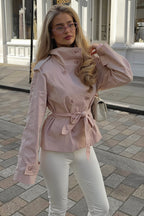 Lila Pink double-breasted short jacket styled with the belt tied at the waist and white trousers on a cobblestone street.