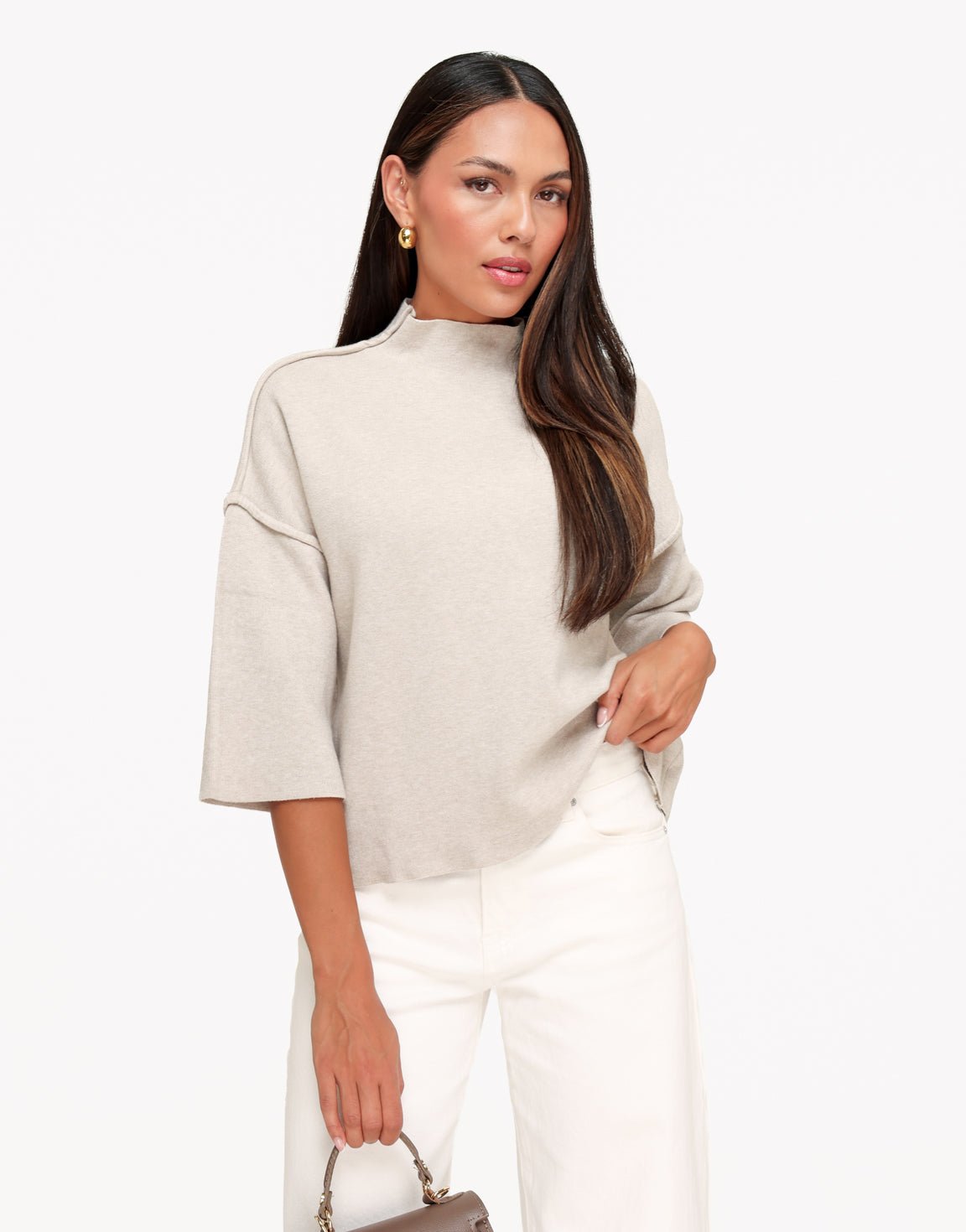 Linnea Taupe high neck knit top styled with white wide-leg pants, shown from the front with one hand at the hip.