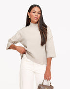Linnea Taupe high neck knit top with relaxed dropped shoulders and three-quarter sleeves, styled with white pants and a brown handbag.