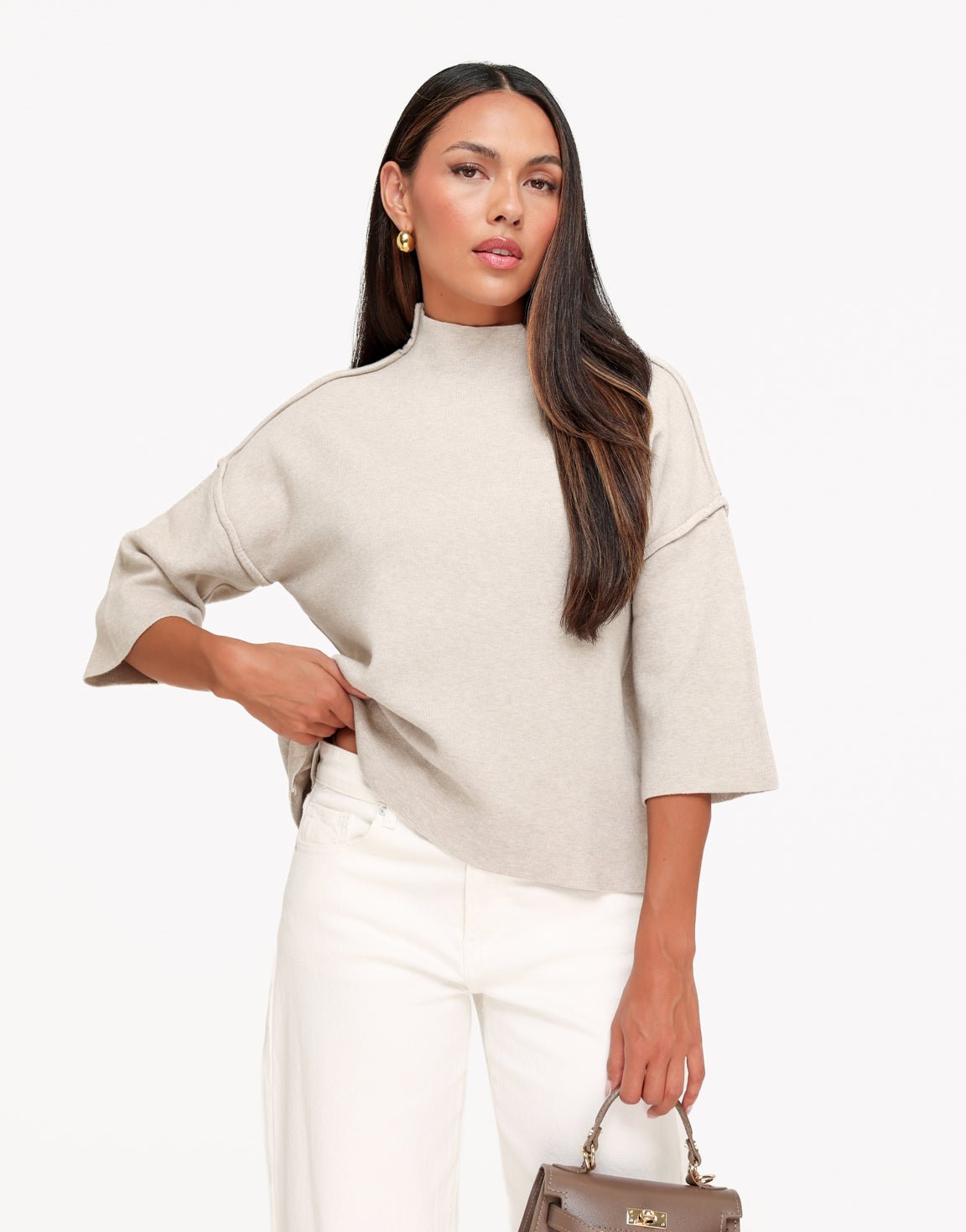 Linnea Taupe high neck knit top with relaxed dropped shoulders and three-quarter sleeves, styled with white pants and a brown handbag.