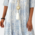 Close-up detail of the Liora Midi Dress Paisley-Print Tiered Tassel-Tie in blue, showcasing the intricate paisley print, gathered tiered construction, lightweight fabric, and decorative tassel-tie neckline. Designed by Bella Hudson.