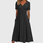 Front view of the Marisol Summer Midi Dress Ruched V-Neck in black, featuring a ruched crossover bodice, V-neckline, short sleeves, flowing midi silhouette, and convenient side pockets. Designed by Bella Hudson.
