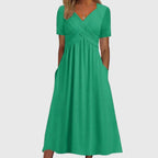 Front view of the Marisol Summer Midi Dress Ruched V-Neck in green, showcasing a ruched crossover bodice, elegant V-neckline, short sleeves, flowing midi skirt, and functional side pockets. Designed by Bella Hudson.