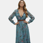 Posing view of the Marlena Maxi Dress Floral-Embroidered Long-Sleeve Boho in blue, featuring the embroidered floral pattern, deep V-neckline, long sleeves, and flowing bohemian design. Designed by Bella Hudson.