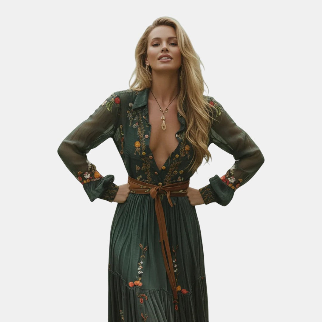 Posing view of the Marlena Maxi Dress Floral-Embroidered Long-Sleeve Boho in green, featuring a deep V-neckline, braided waist belt, long sleeves, and flowing boho-inspired styling. Designed by Bella Hudson.