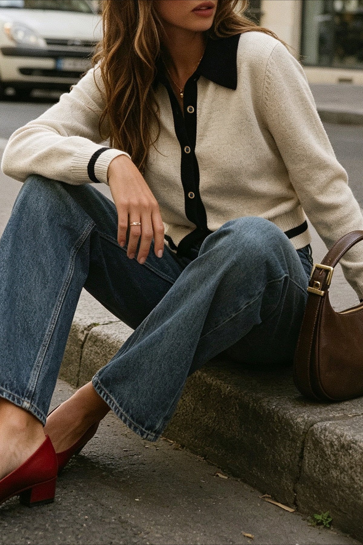 Mia Off White knit cardigan worn seated on a curb with wide-leg jeans, red heels, and a brown bag, showing the buttoned front and contrast trim.
