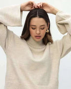 Mila Beige mock-neck sweater styled with hands raised, showing the flared sleeves and ribbed hem.