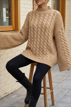 Mila Khaki cable-knit mock-neck sweater with flared sleeves styled with black leggings while seated on a stool.