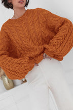 Mila Orange cable-knit crewneck sweater shown close up with oversized cable sleeves.