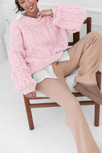 Mila Pink cable-knit sweater worn over a white shirt while seated on a wooden chair.