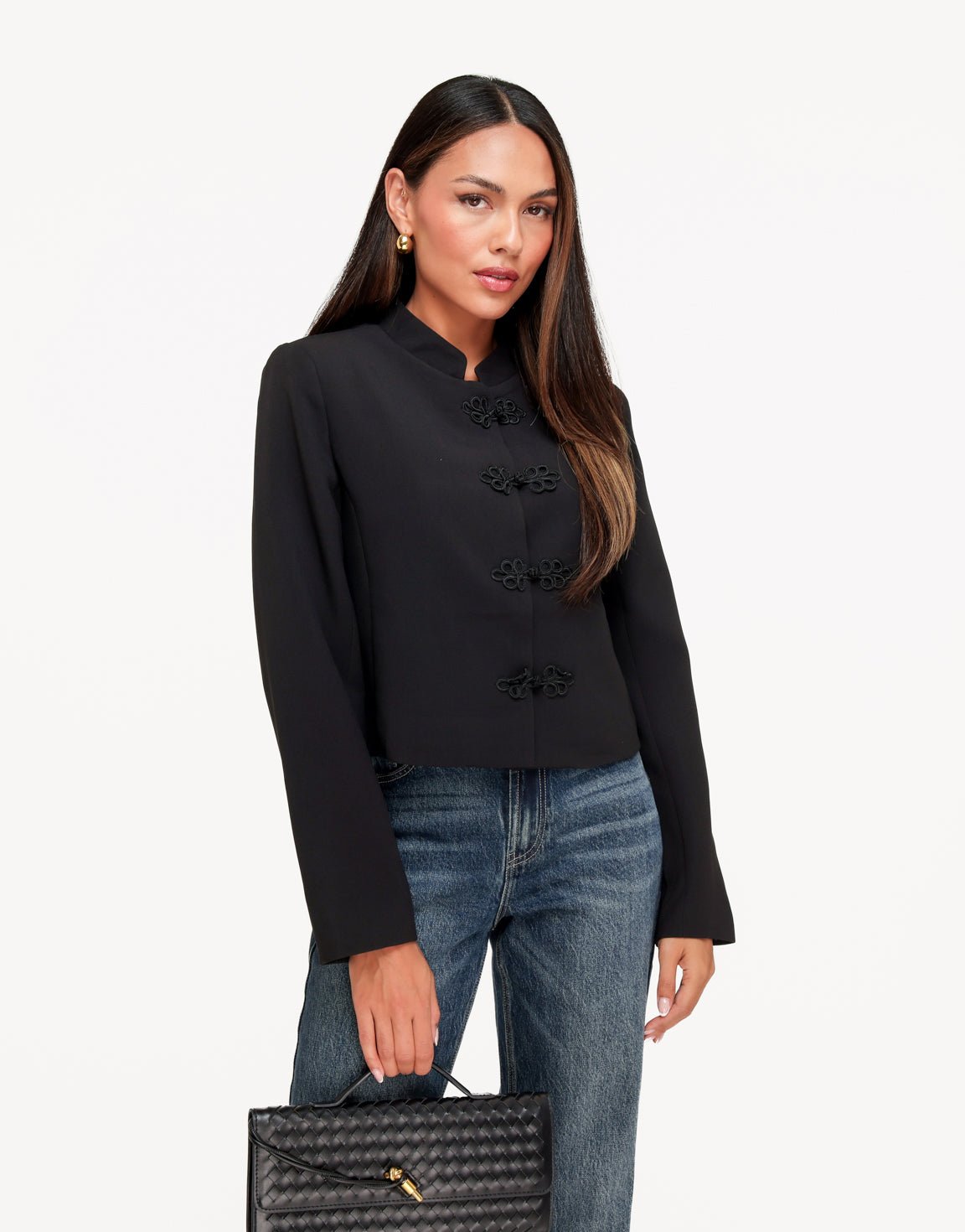 Mirella Black cropped jacket with stand collar and frog closures styled with blue jeans and a woven black handbag.