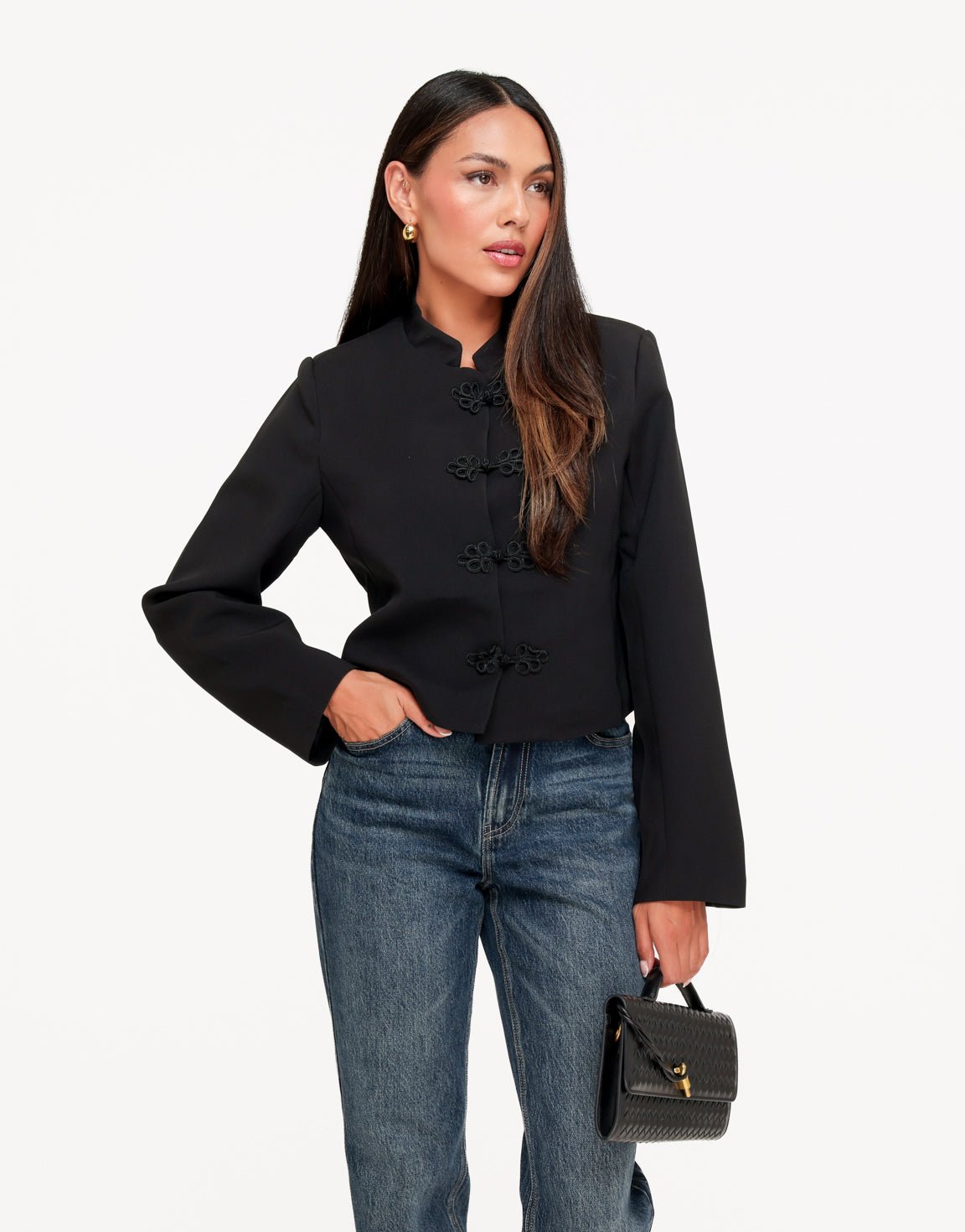 Mirella Black cropped jacket worn with one hand in the jeans pocket, showing the frog closures and flared cuffs.