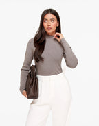 Mirelle Gray ribbed knit sweater styled with white trousers, with the model's hand at her neckline.