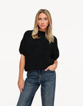 Nadine Black high neck knit sweater worn with a hand in the pocket of dark wash jeans, shown from the front.