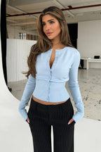 Nina Blue knit cardigan in a light sky blue shade with hands in pockets of pinstripe pants.