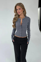 Nina Dark Gray knit cardigan with hands in the pockets of black pinstripe pants in a studio.