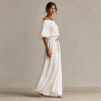 Side view of the Noa Off-Shoulder Lightweight Linen Maxi Dress in white featuring an off-shoulder neckline, lantern sleeves, adjustable waist tie, and flowing maxi-length silhouette. Designed by Bella Hudson.