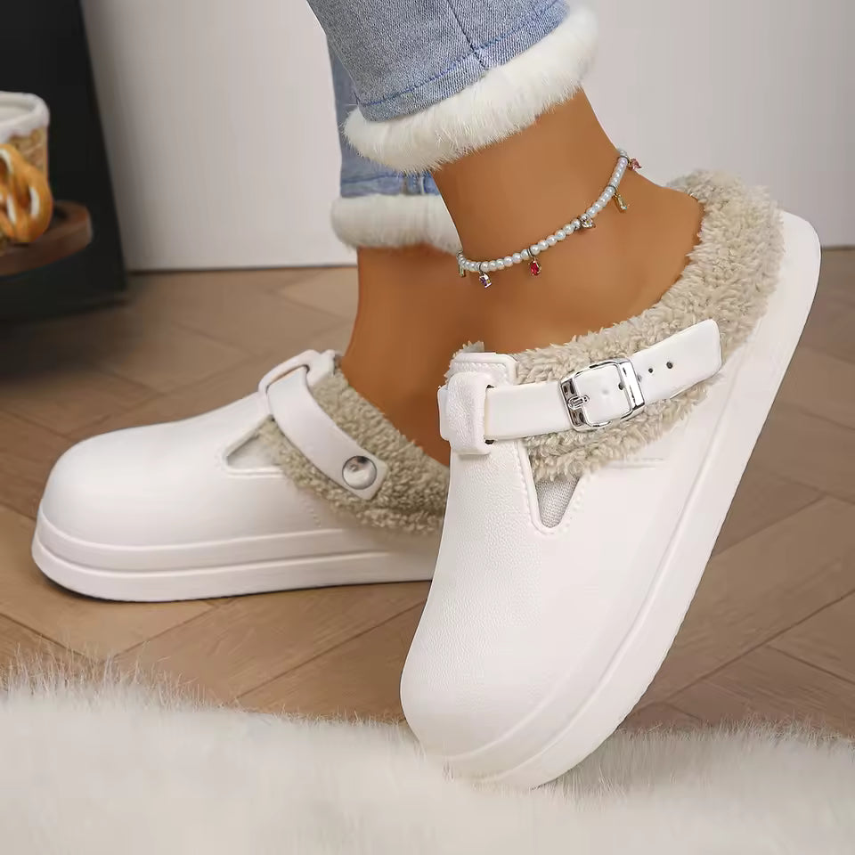 Paige White mule slippers with plush faux-fur lining, decorative buckle straps, rounded closed toes, and thick soles, shown on feet