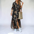 Lifestyle view of the Rosamund Shirt Dress Printed Long-Sleeve Button-Front in black, showcasing the relaxed maxi silhouette, chain print, side slit, and collared button-front design. Designed by Bella Hudson.