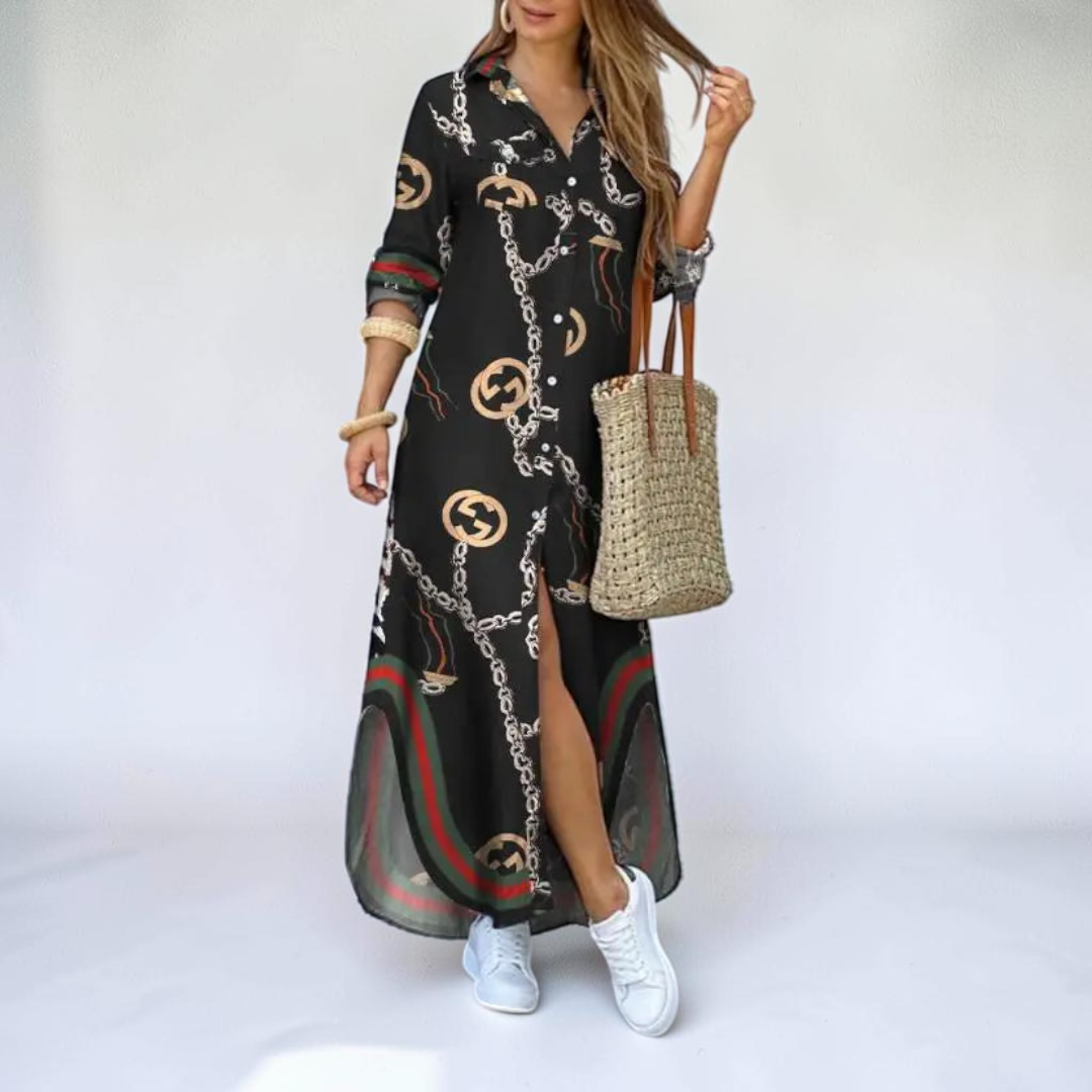 Lifestyle view of the Rosamund Shirt Dress Printed Long-Sleeve Button-Front in black, showcasing the relaxed maxi silhouette, chain print, side slit, and collared button-front design. Designed by Bella Hudson.