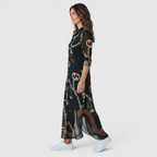 Side view of the Rosamund Shirt Dress Printed Long-Sleeve Button-Front in black, showcasing the collared neckline, chain print, side slit, and flowing maxi-length silhouette. Designed by Bella Hudson.