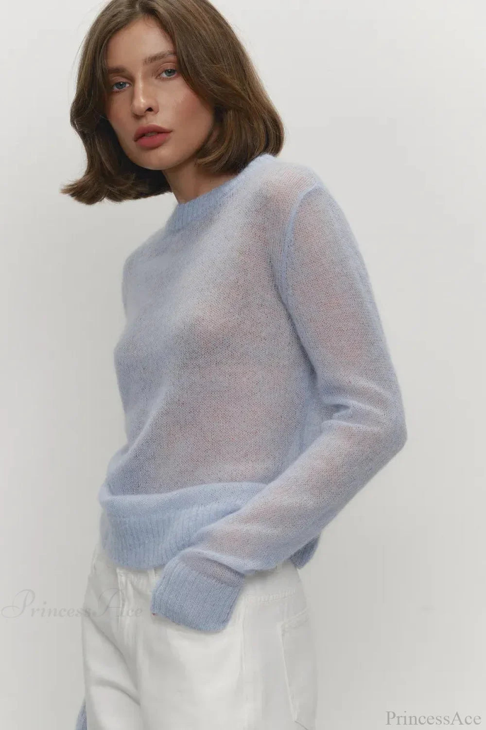 Selena Blue sheer-knit crewneck sweater shown from a side angle with white pants and ribbed cuffs.